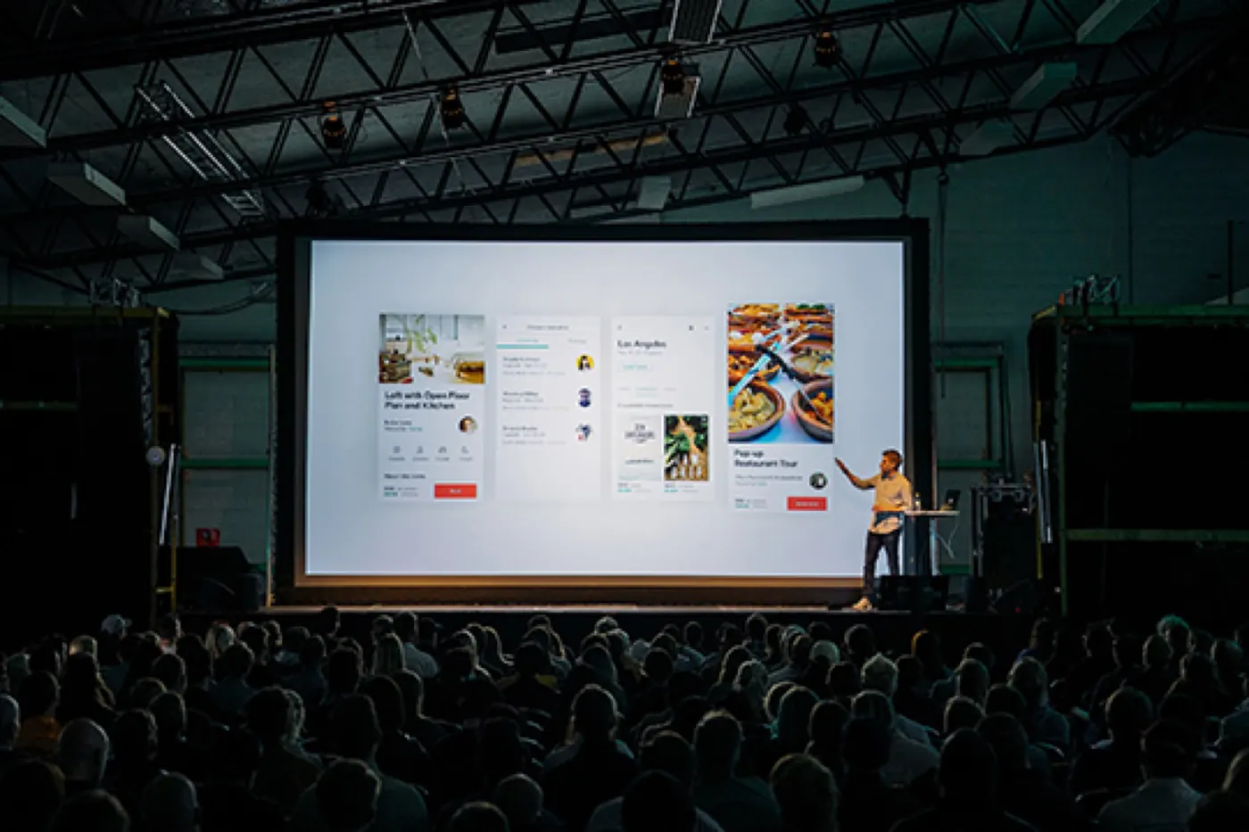 A speaker presenting on a large stage to a full software testing conference audience